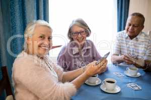 Smiling senior friends playing cards while having coffee