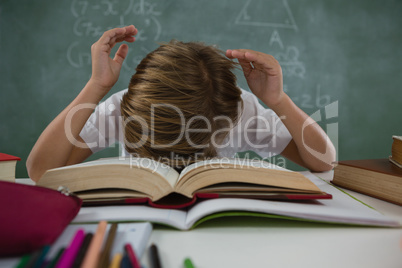 Schoolboy lying on open books in classroom
