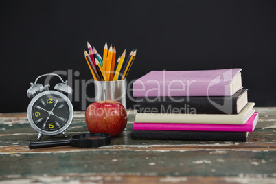 Stack of books with alarm clock, apple, magnifying glass and pen holder