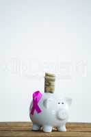 Paper currency and pink Breast Cancer Awareness ribbon on piggybank over wooden table