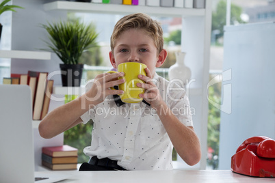 Portrait of businessman drinking coffee from yellow mug at desk