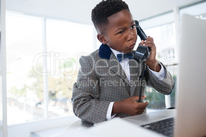 Confused businessman talking on telephone while looking at laptop