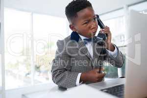 Confused businessman talking on telephone while looking at laptop