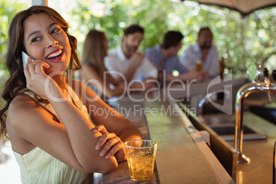 Smiling woman talking on mobile phone while having a glass of beer in restaurant