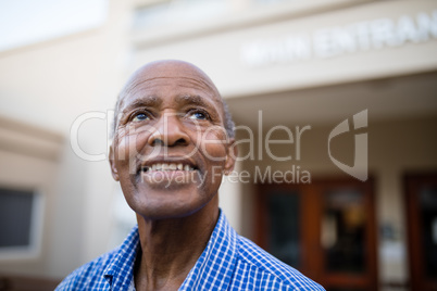 Thoughtful senior man smiling while looking up at nursing home