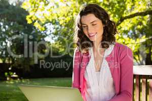 Woman sitting on bench and using laptop in garden on a sunny day