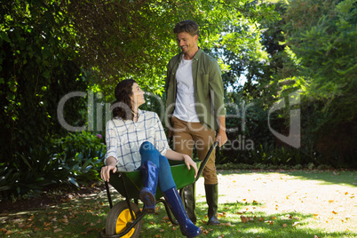 Man interacting with woman while pushing wheelbarrow in garden