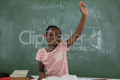 Schoolgirl raising hand while sitting in classroom