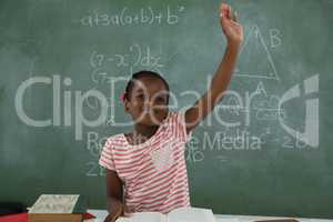 Schoolgirl raising hand while sitting in classroom