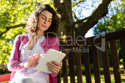 Woman sitting on bench and using digital tablet in garden