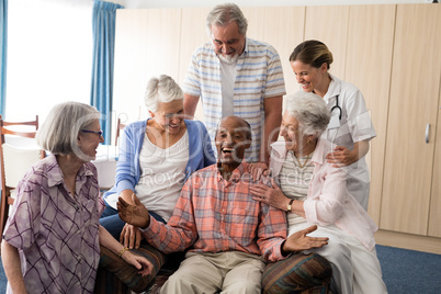 Cheerful senior man with friends and practitioner on sofa