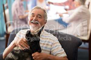 Portrait of smiling senior man sitting with puppy on chair