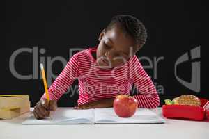 Schoolgirl doing her homework against black background
