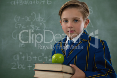 Schoolboy holding books stack with apple against chalkboard