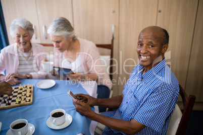 Smiling senior man using mobile phone while having tea with friends