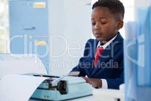 Boy imitating as businessman using typewriter in office