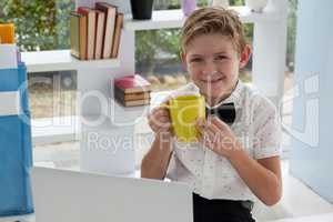 Portrait of businessman drinking coffee from yellow mug by laptop