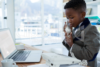 Smiling businessman with laptop using telephone at desk