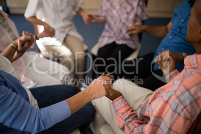 High angle view of seniors and female doctor holding hands while sitting on chairs