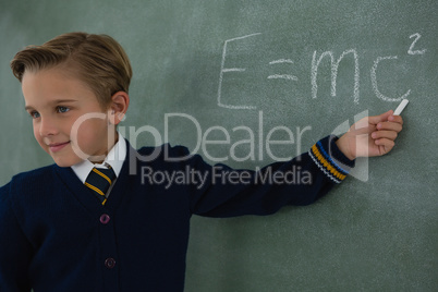 Schoolboy solving maths formula on chalkboard