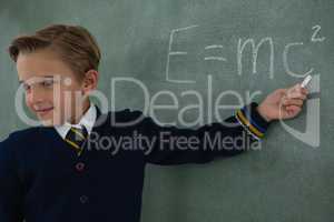 Schoolboy solving maths formula on chalkboard