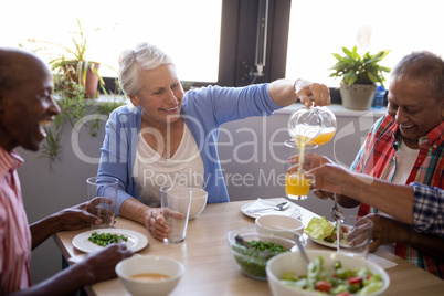 Smiling senior woman serving juice to friends