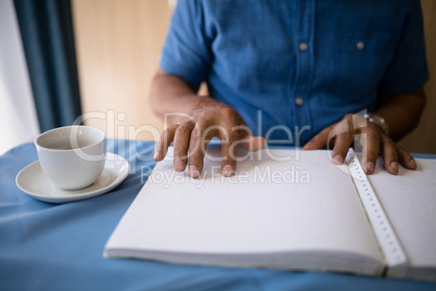 Midsection of senior man reading book by coffee cup at table