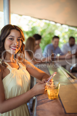 Smiling woman using mobile phone while having a glass of beer in restaurant