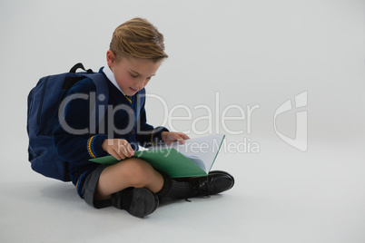 Schoolboy reading book while sitting on white background