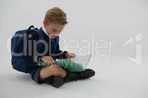 Schoolboy reading book while sitting on white background