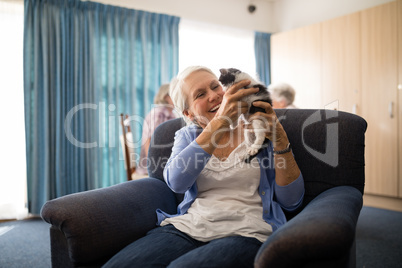 Cheerful senior woman holding kitten while sitting on armchair