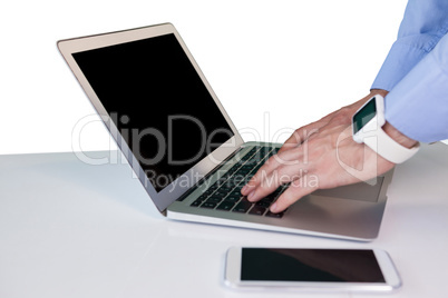 Cropped hand of businessman wearing smart watch while using laptop at table