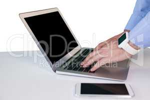 Cropped hand of businessman wearing smart watch while using laptop at table