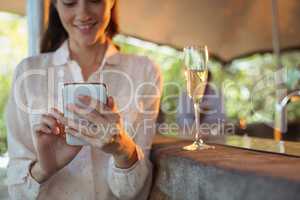 Smiling woman using mobile phone while having a glass of champagne