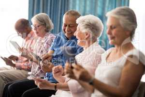 Smiling senior people sitting on chairs while using digital tablets