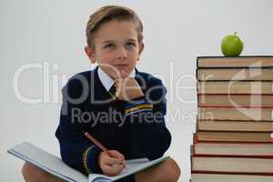 Schoolboy doing his homework while sitting beside books stack