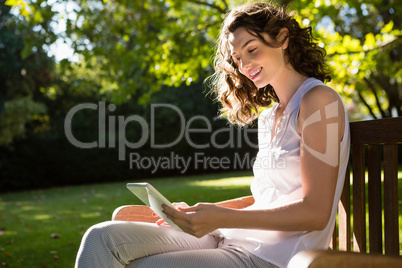 Woman sitting on bench and using digital tablet in garden on a sunny day