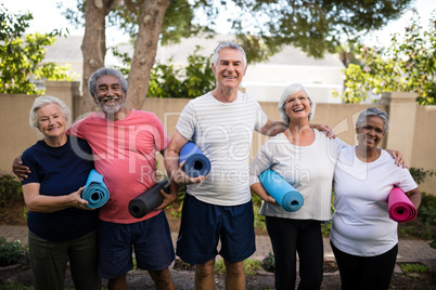 Portrait of laughing senior friends carrying exercise mats at park