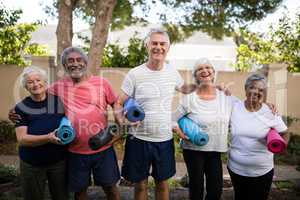 Portrait of laughing senior friends carrying exercise mats at park