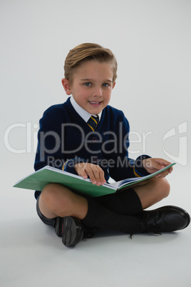 Schoolboy reading book while sitting on white background