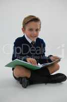 Schoolboy reading book while sitting on white background