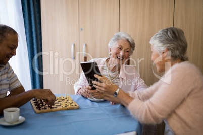 Smiling friends playing chess and using technology