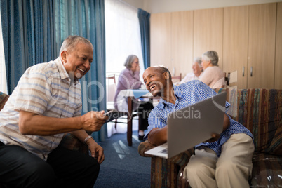 Happy senior man showing laptop to friend