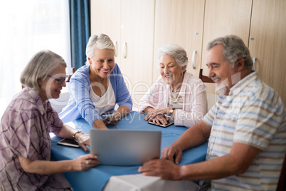 Smiling senior man showing laptop to women at table