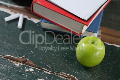 Books, green apple and chalk on wooden table