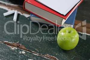 Books, green apple and chalk on wooden table