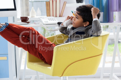 Businessman talking on landline phone while sitting on armchair