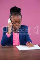Businesswoman talking on mobile phone while reading report