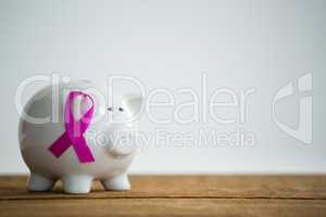 Close-up of pink Breast Cancer Awareness ribbon on piggybank over wooden table