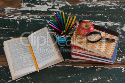 Stack of books with apple, magnifying glass and pen holder
